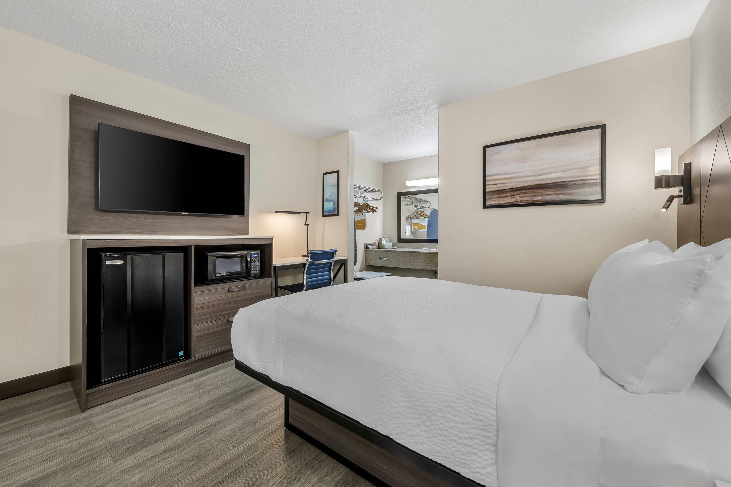 A hotel room with a bed, a flat-screen TV, a minibar, a desk, and a mirror.