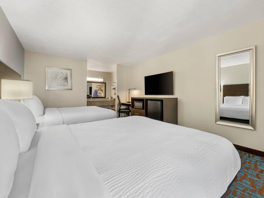 A hotel room with two beds, a desk, a flat-screen TV, a mirror, and a framed picture on the wall.