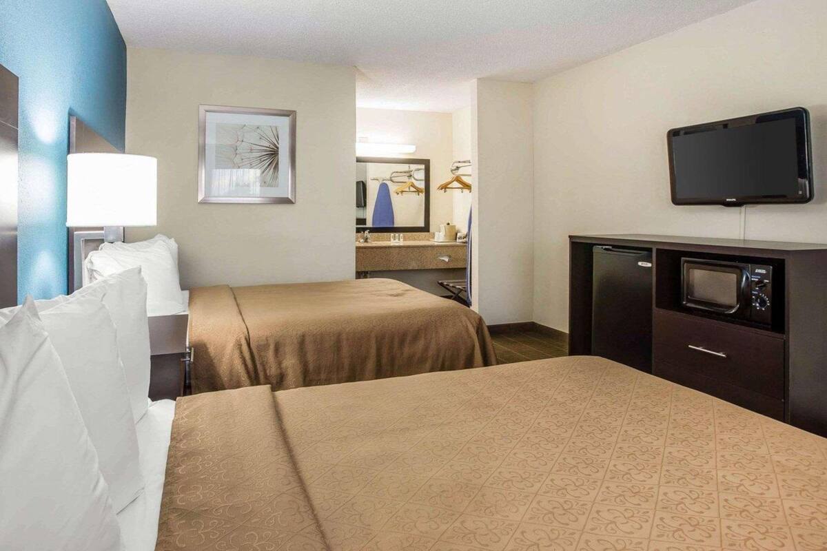 Ett hotellrum med två sängar, ett skrivbord med en tv, en spegel och ett badrum som syns i bakgrunden.