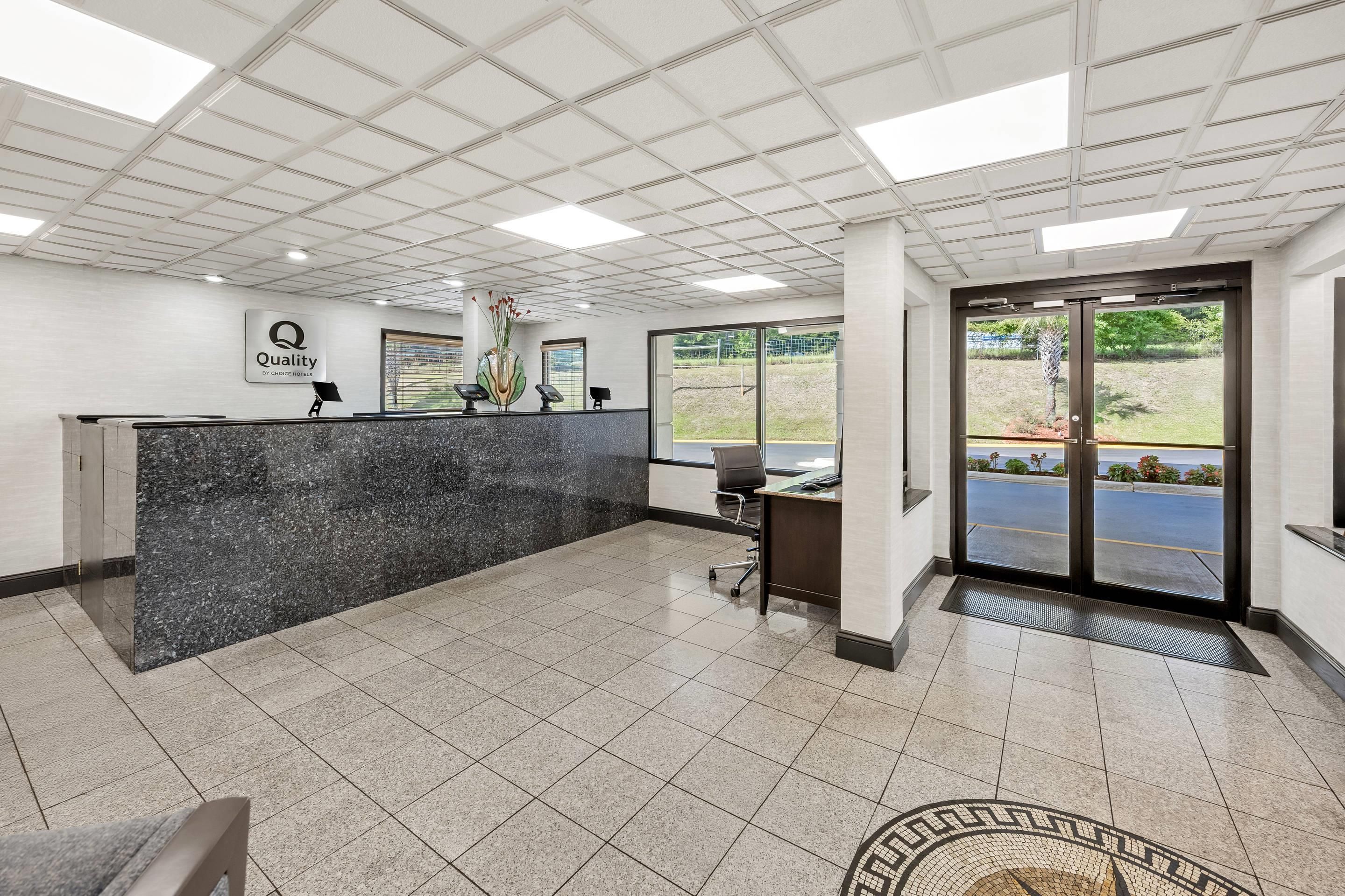 A hotel reception area with a marble counter, a sign indicating 'Quality by Choice Hotels', and a view of the outdoors through large windows.