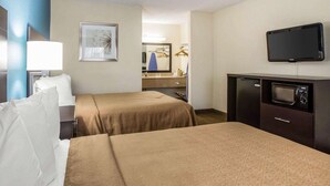 A hotel room with two beds, a desk with a television, a mirror, and a bathroom visible through an open door.