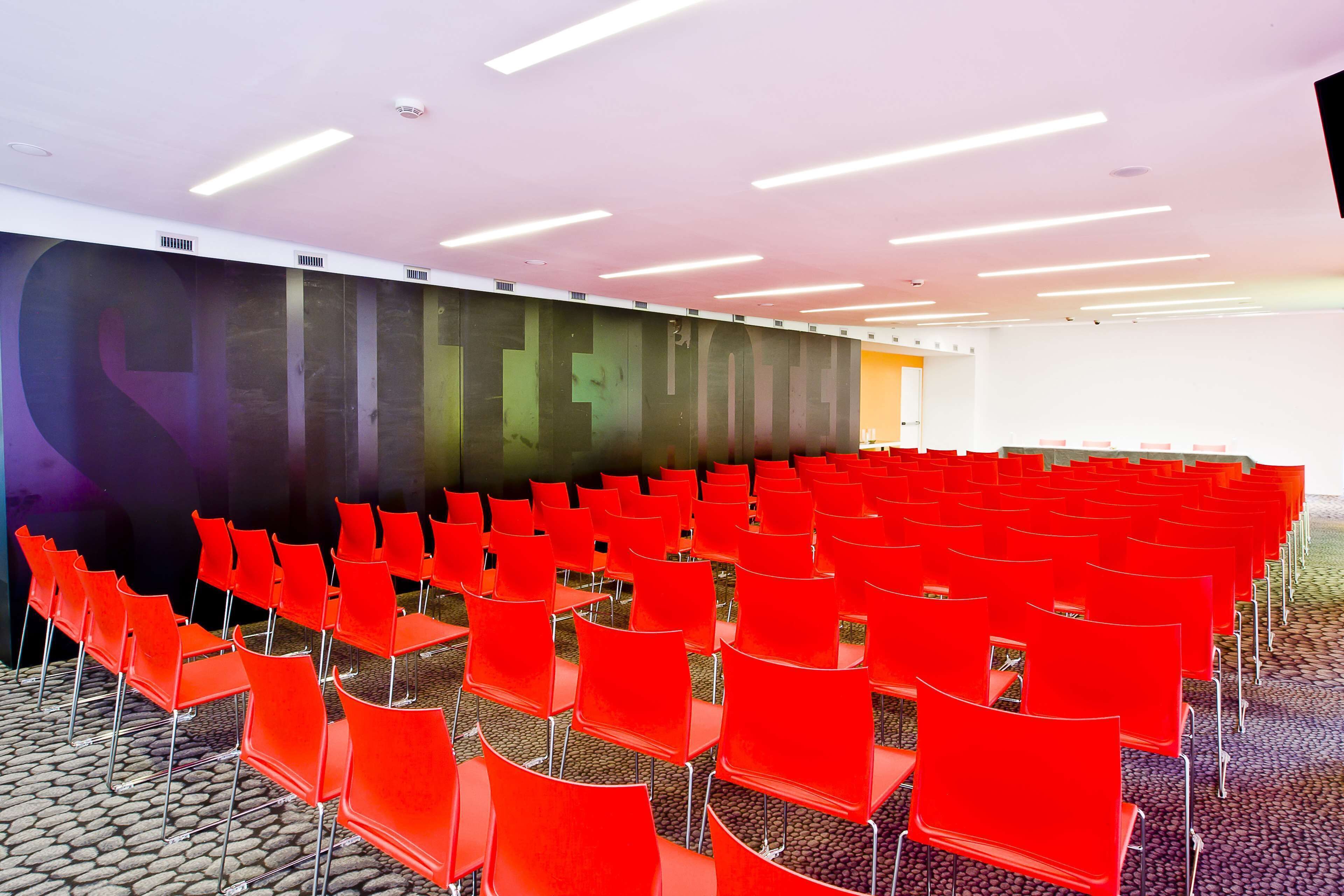 A conference room with rows of red chairs, a large screen, and a modern ceiling design.