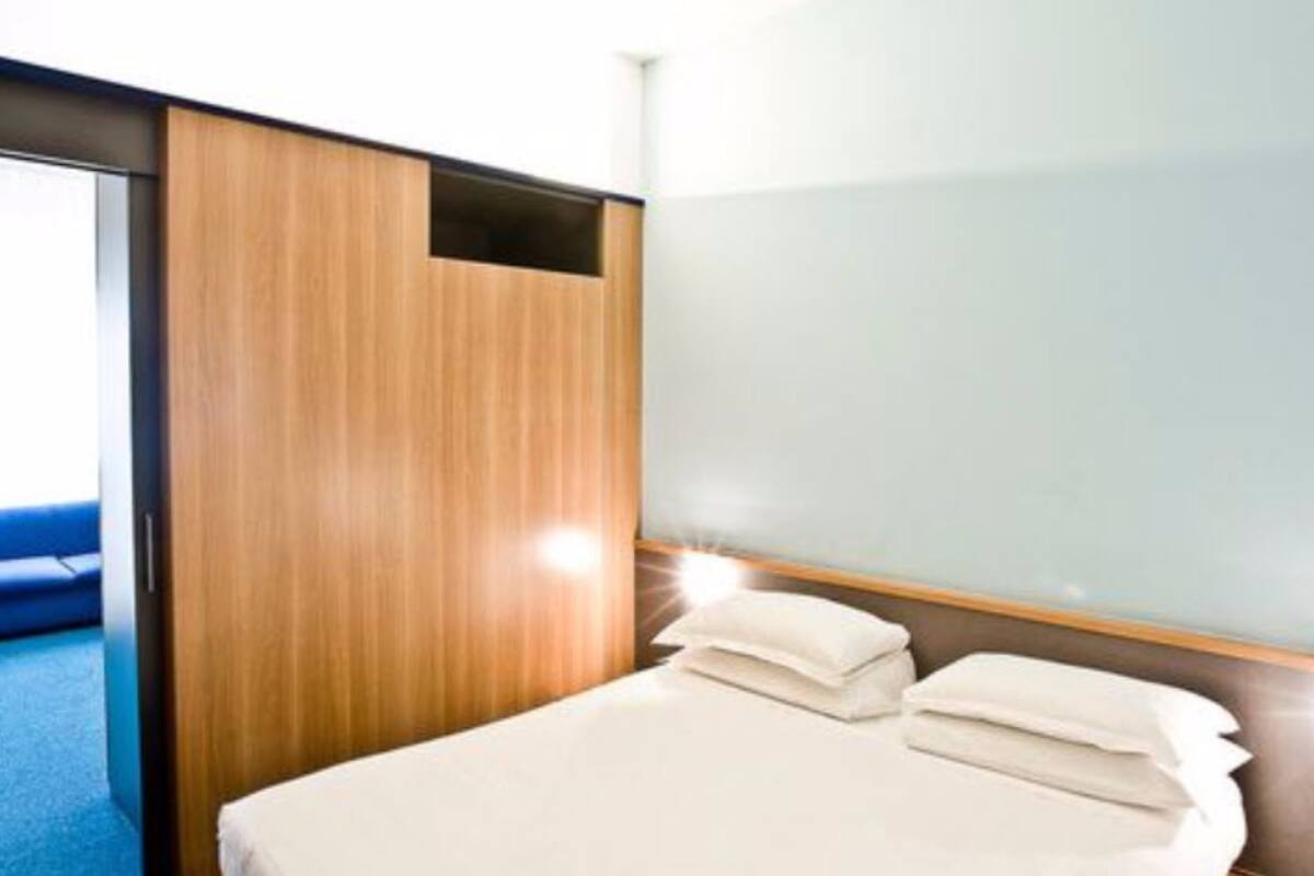 Una habitación de hotel con una cama, un armario de madera y una silla azul.