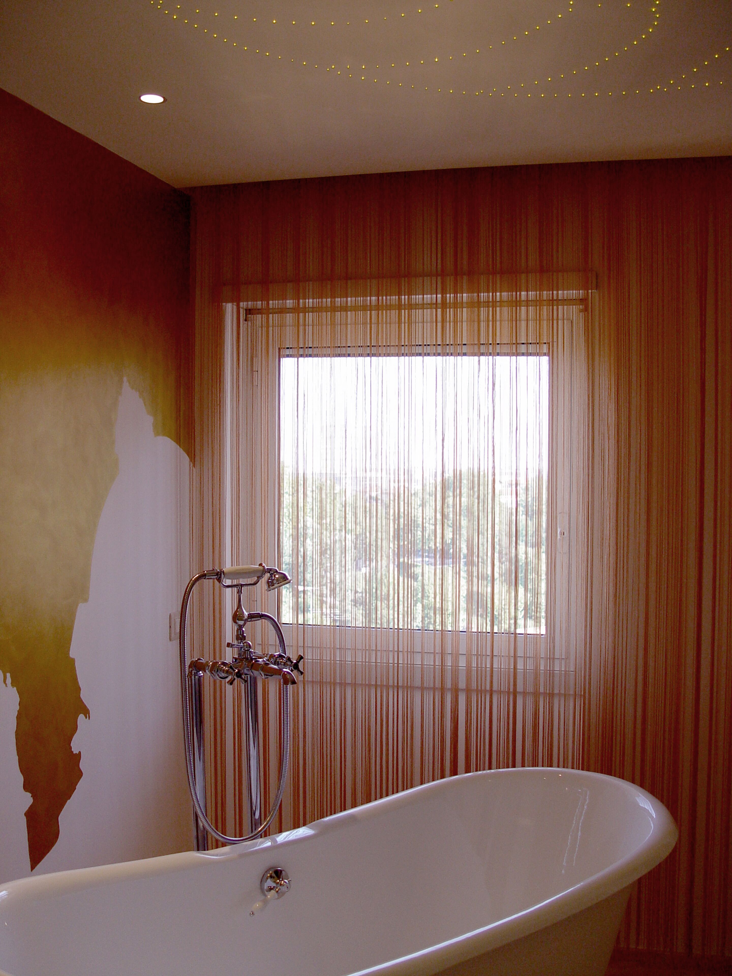 Un bagno con una vasca freestanding, una finestra con persiane verticali e un soffitto decorato con luci a stringa.