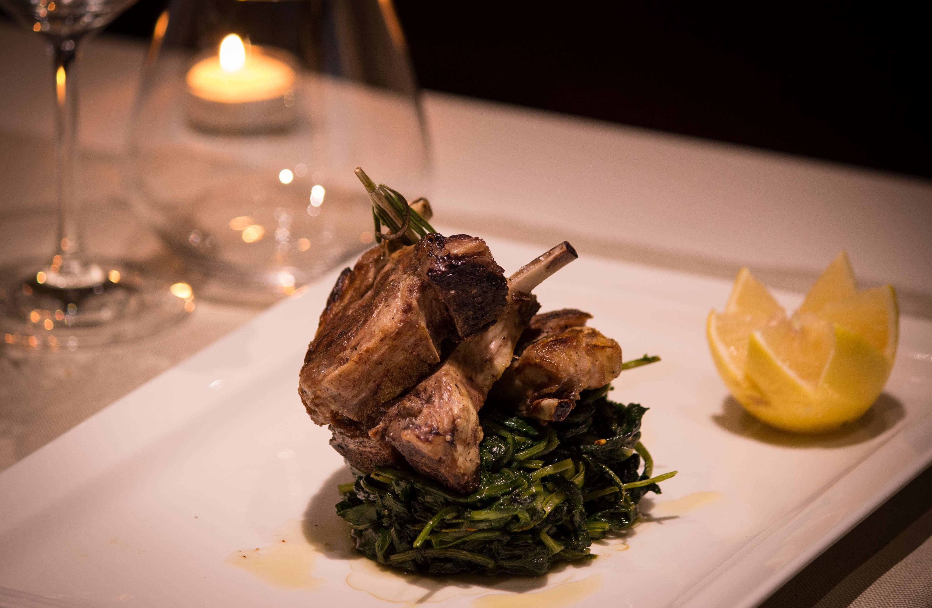 A plate with roasted lamb, greens, and a lemon wedge.