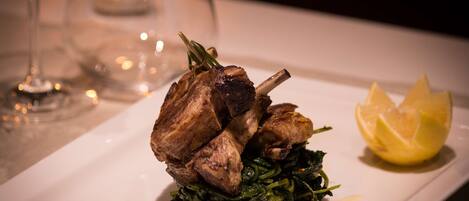 A plate with roasted lamb, greens, and a lemon wedge.