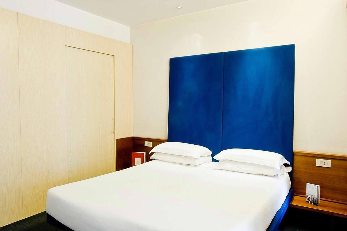 Habitación de hotel con una cama grande, un armario de madera y un cabecero azul.