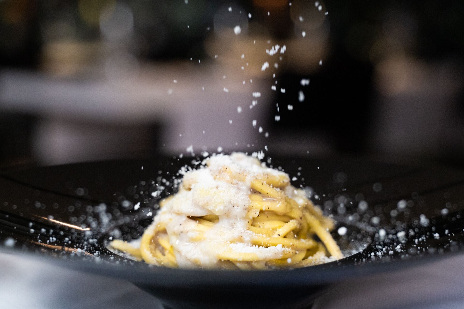 A close-up of a dish with pasta and grated cheese being sprinkled on it.