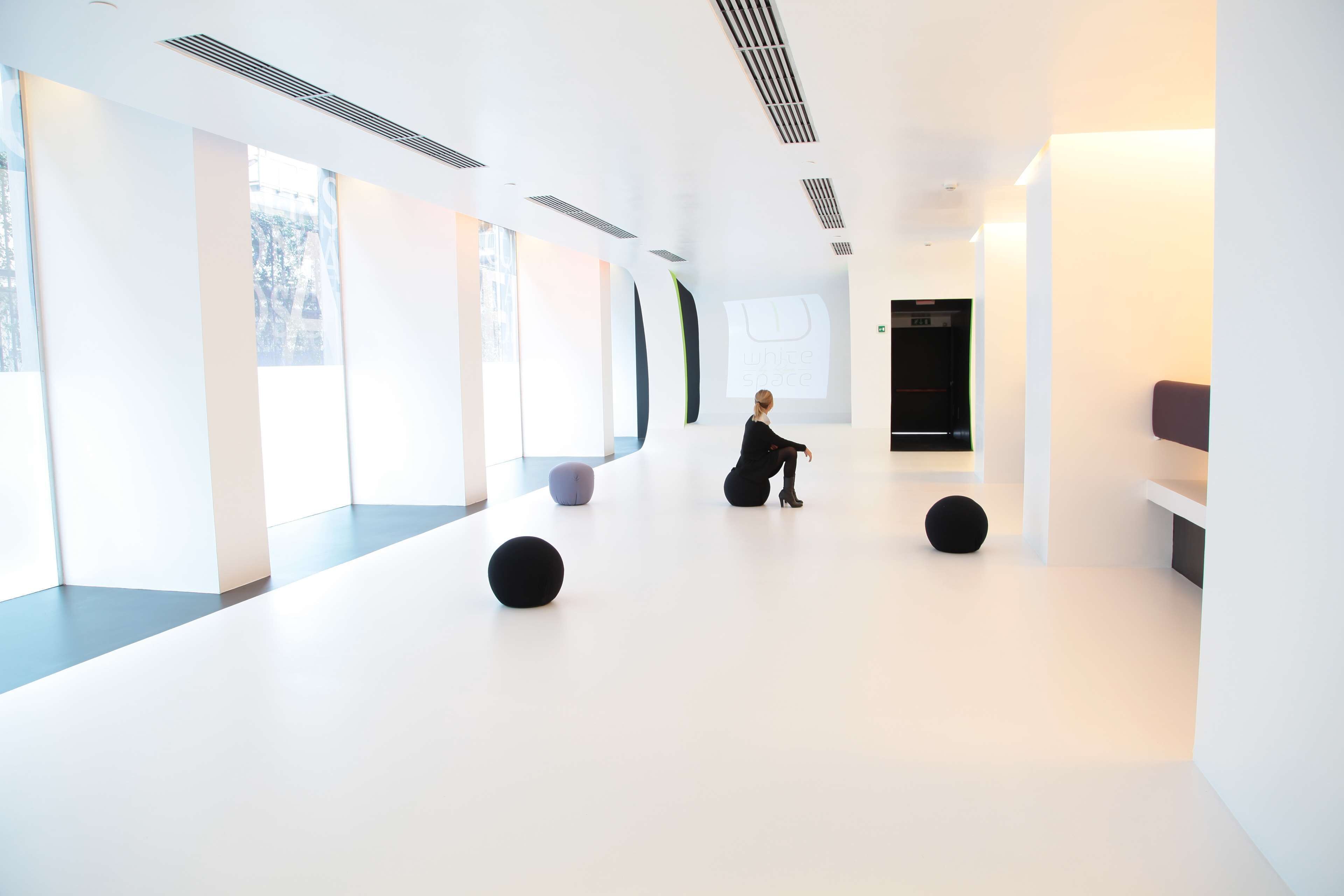A spacious, modern interior with large windows, a minimalist design, and a person performing.
