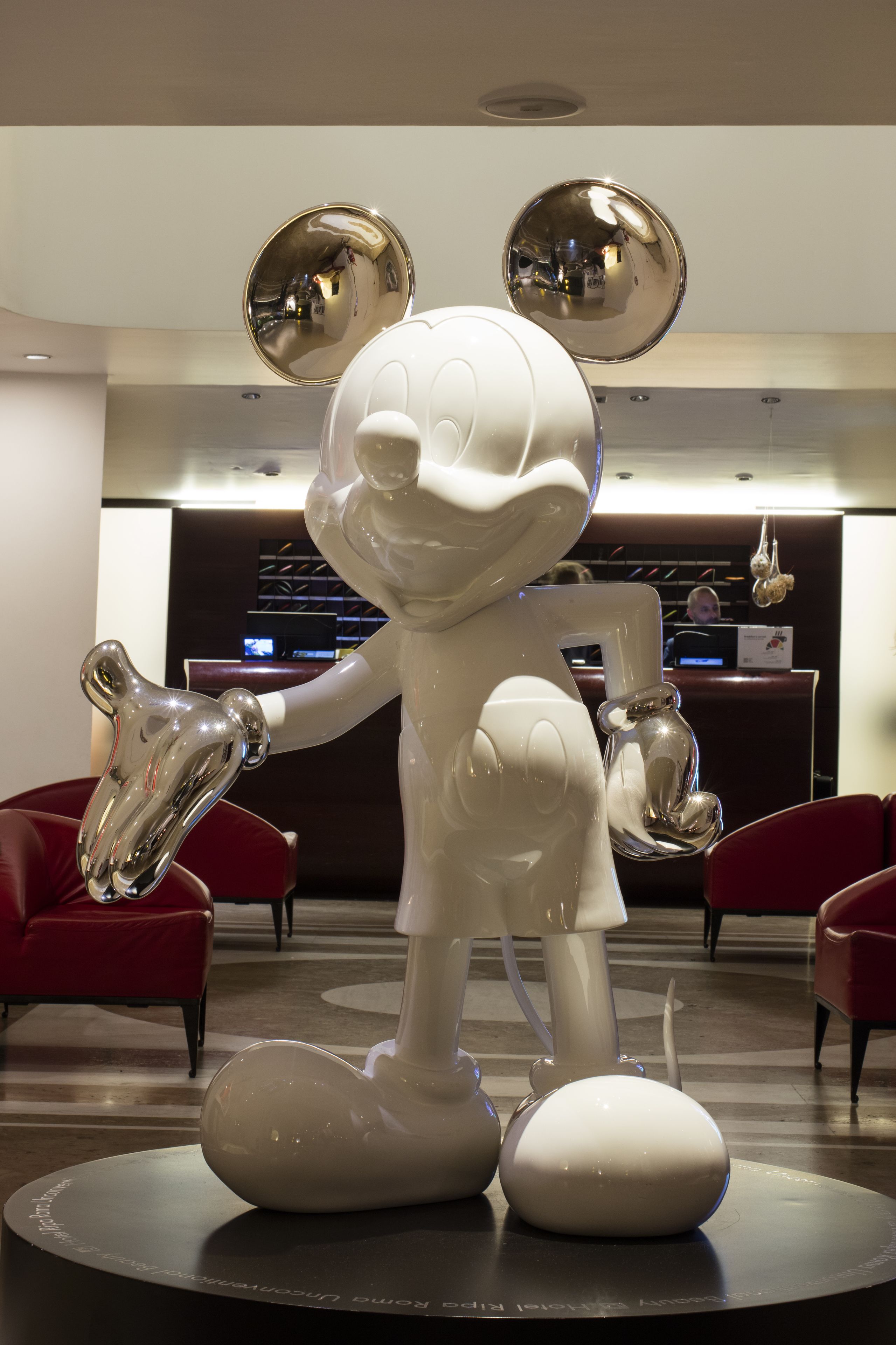 Una gran escultura blanca de un personaje de caricatura en un vestíbulo con sillas rojas y un mostrador de recepción al fondo.