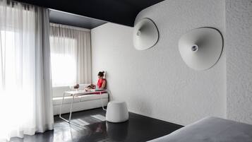 Ein modernes Hotelzimmer mit großem Fenster, einem weißen Sofa, einem kleinen Tisch und einem weißen Pouf.