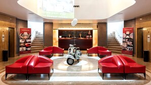 Un vestíbulo de diseño moderno, con una recepción, una escalera y zonas de estar rojas.