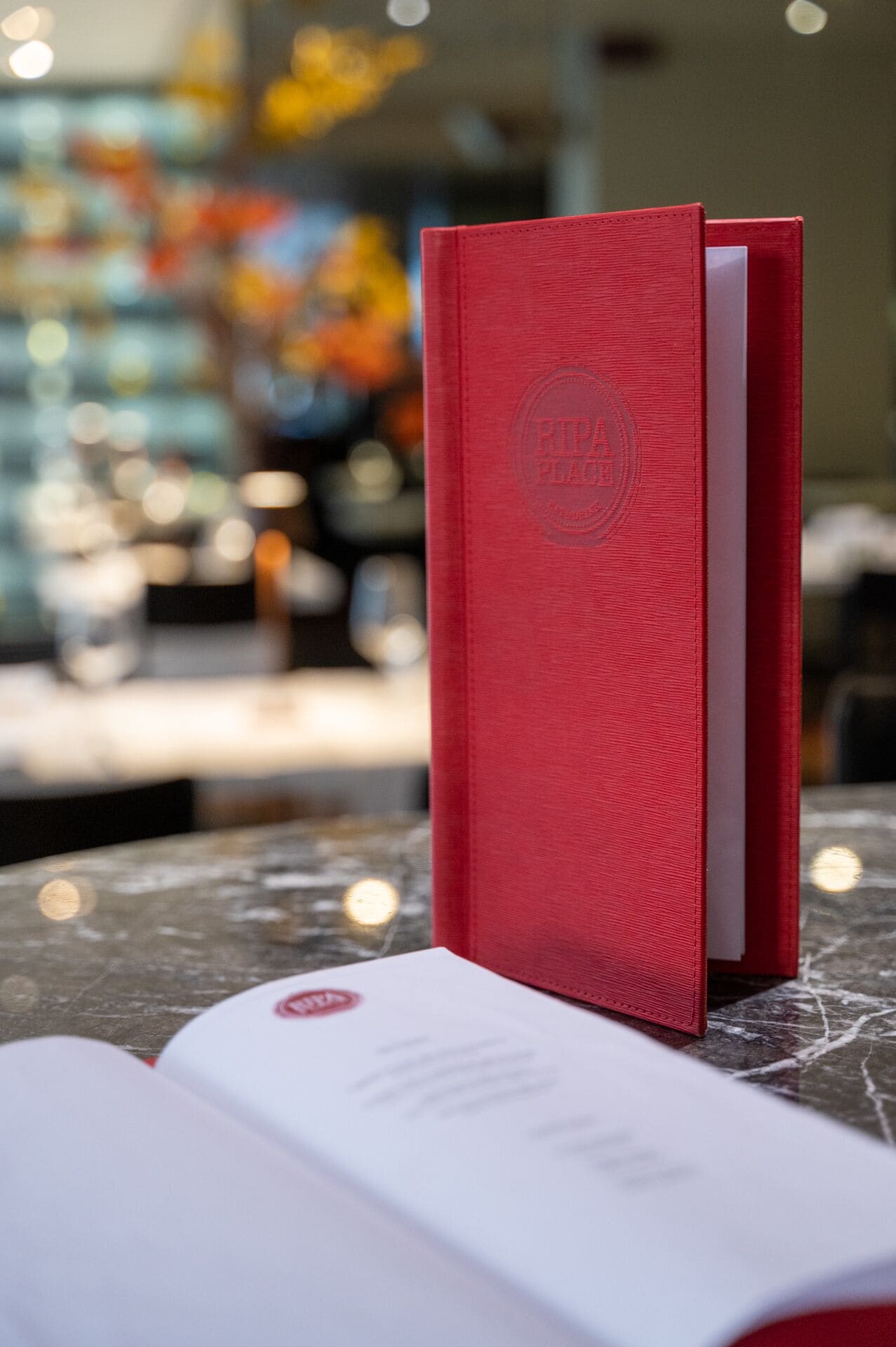 A red book with a visible logo on its cover, placed on a table with a blurred background.