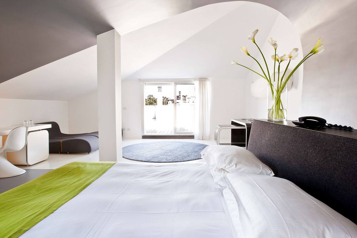 Habitación de hotel moderna con una cama grande, un escritorio, una silla y vistas a la ciudad a través de la ventana.