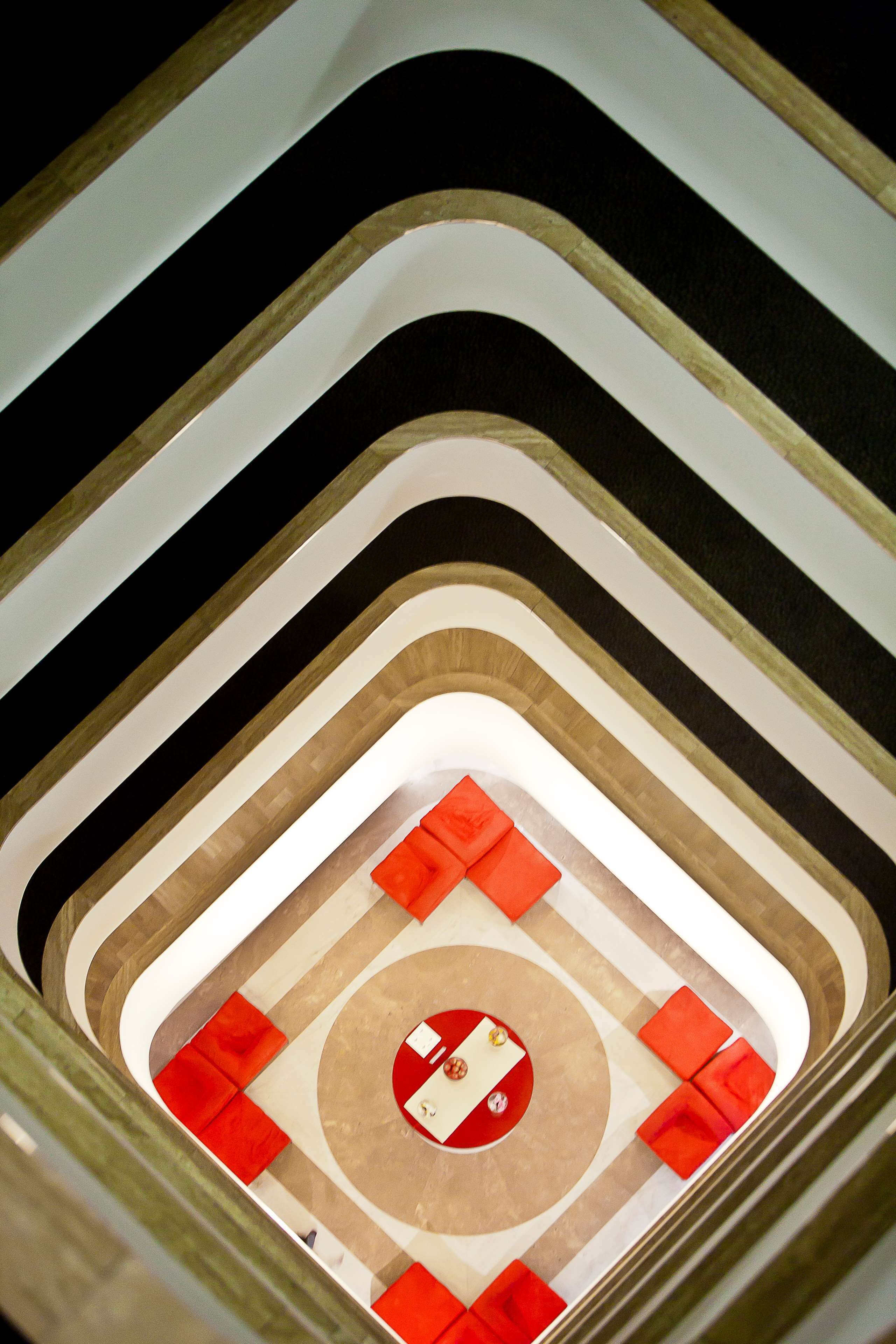Ein mehrgeschossiges Atrium mit einer zentralen, runden Fläche, die rot-weiß gestaltet ist, umgeben von roten Sitzgelegenheiten.