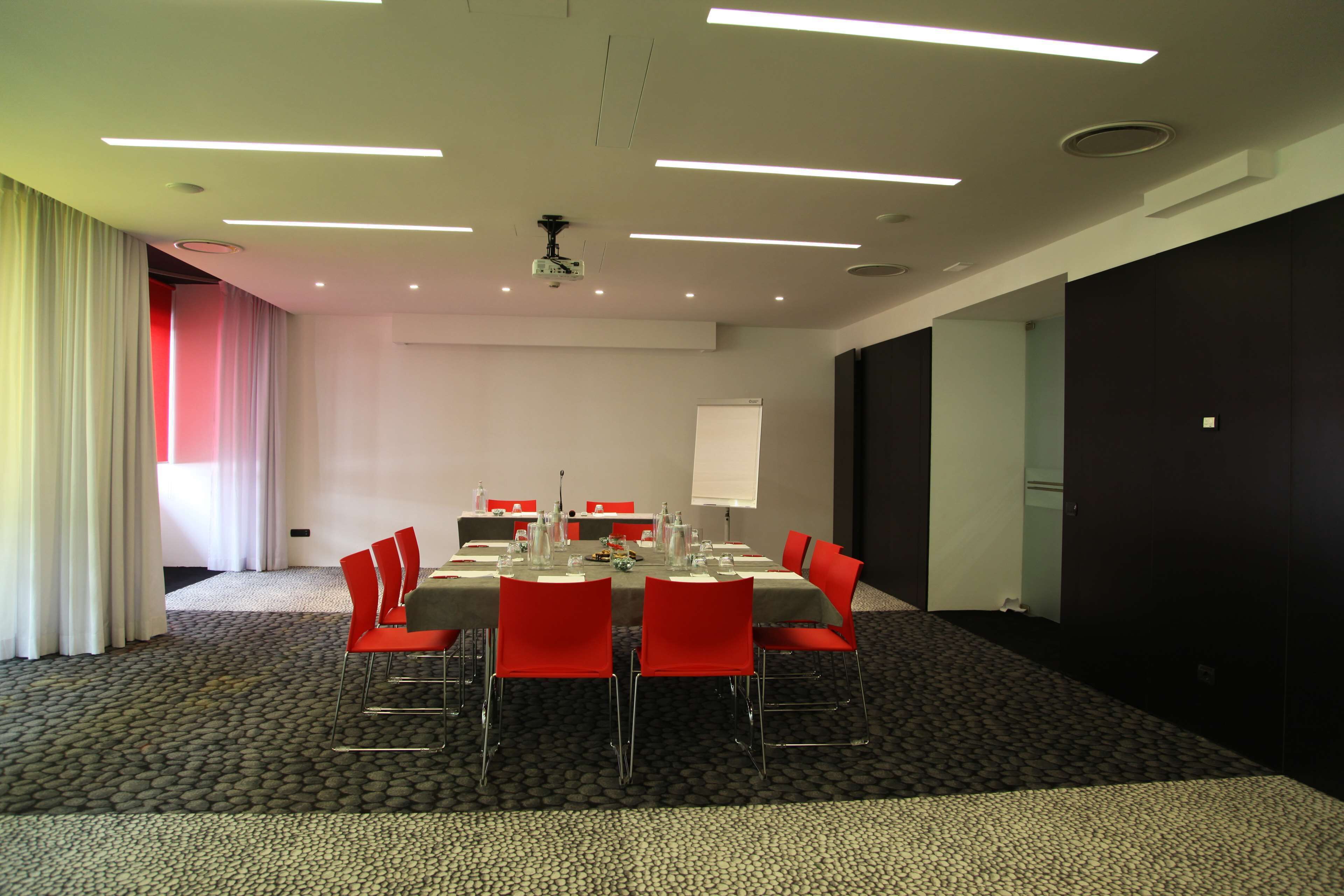 Una sala de conferencias con una mesa dispuesta para una reunión, sillas rojas, un proyector y una pizarra.