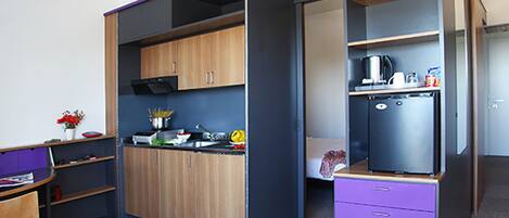 Una cocina compacta con armarios de madera, un refrigerador negro y una pequeña encimera con diversos electrodomésticos.
