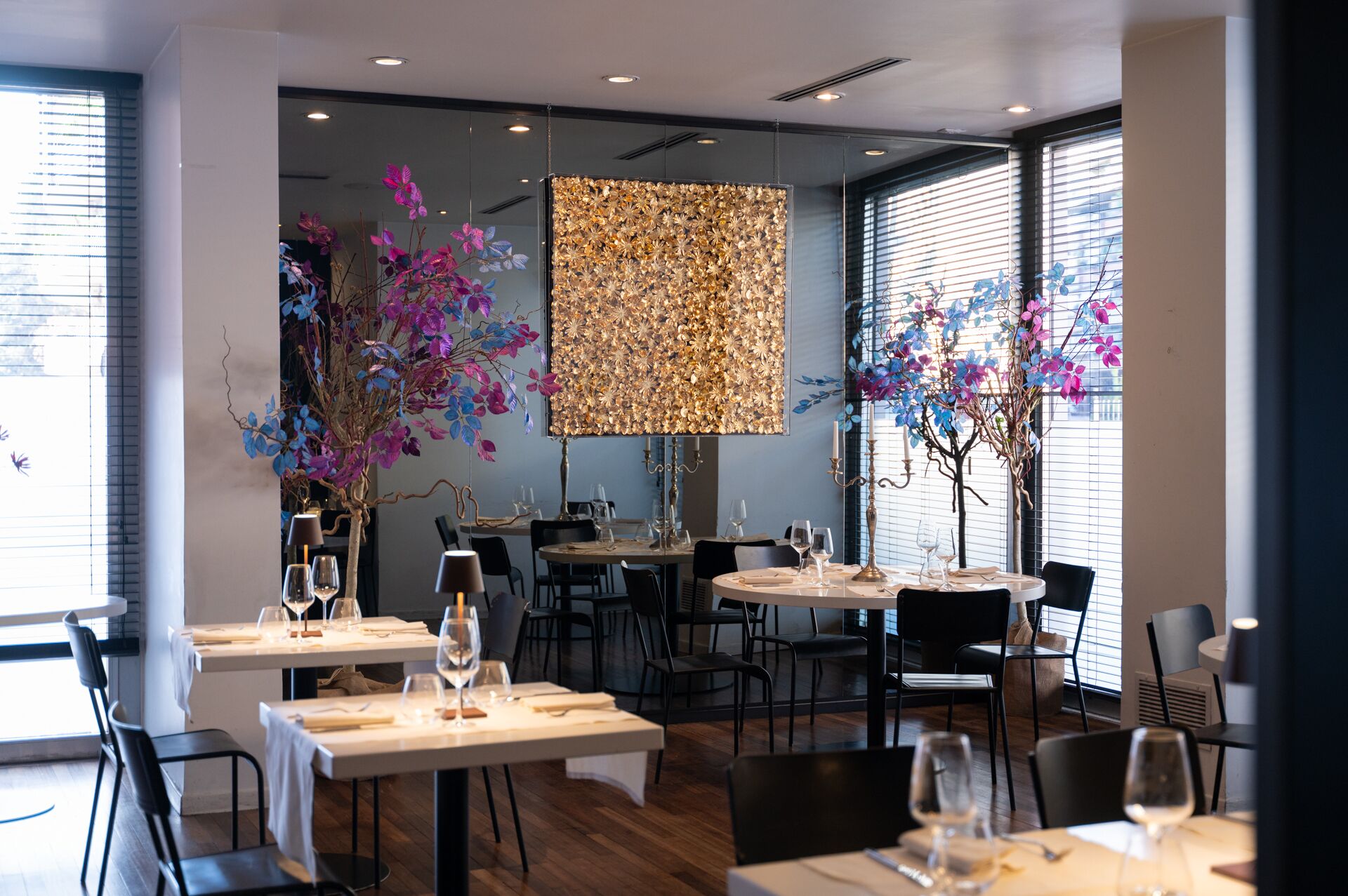 Un intérieur de restaurant moderne avec des tables rondes, des chaises noires et des plantes décoratives.