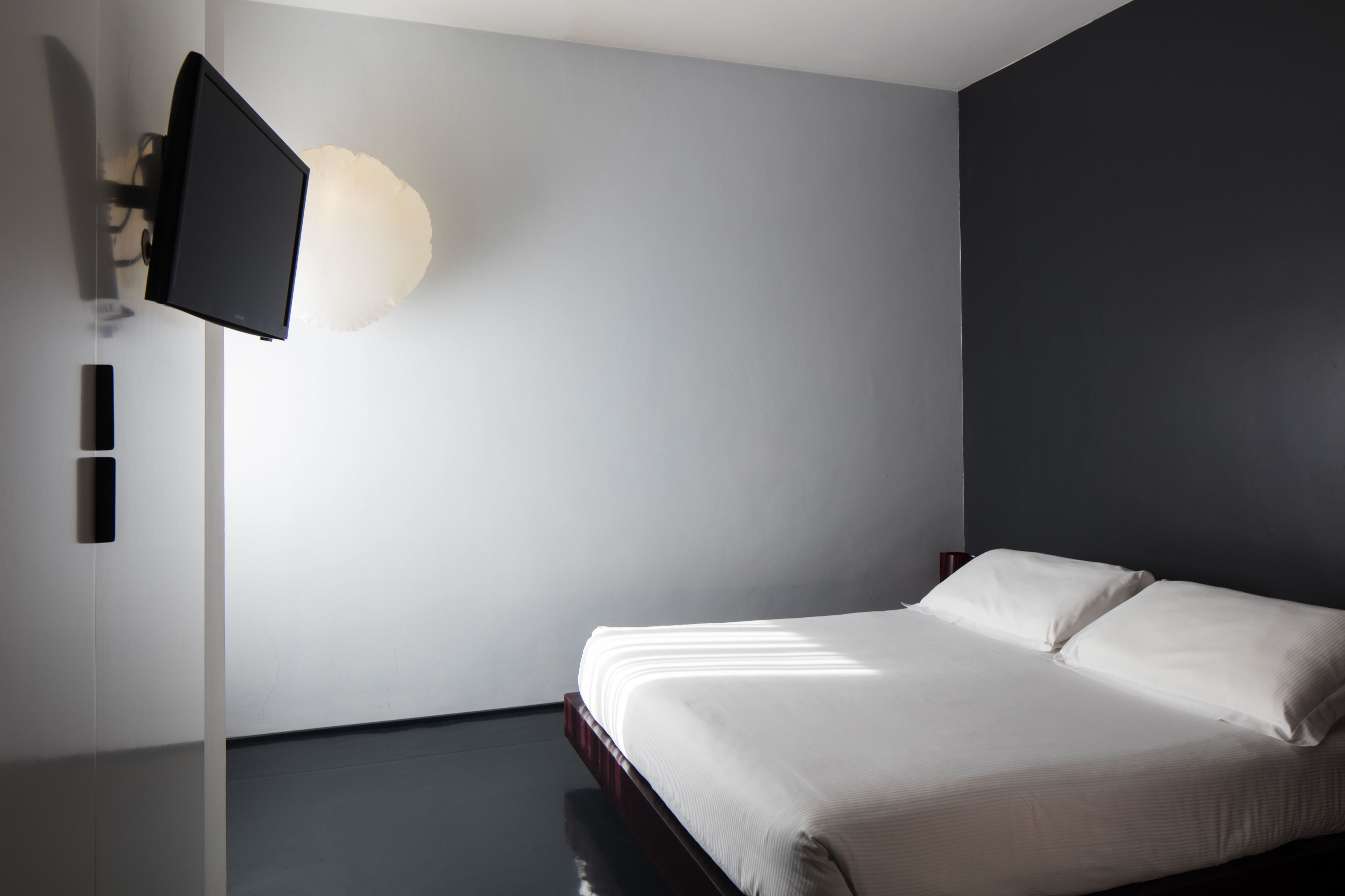 A modern bedroom with a bed, a wall-mounted TV, and a light fixture.
