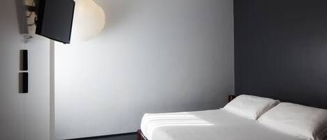A modern bedroom with a bed, a wall-mounted TV, and a light fixture.