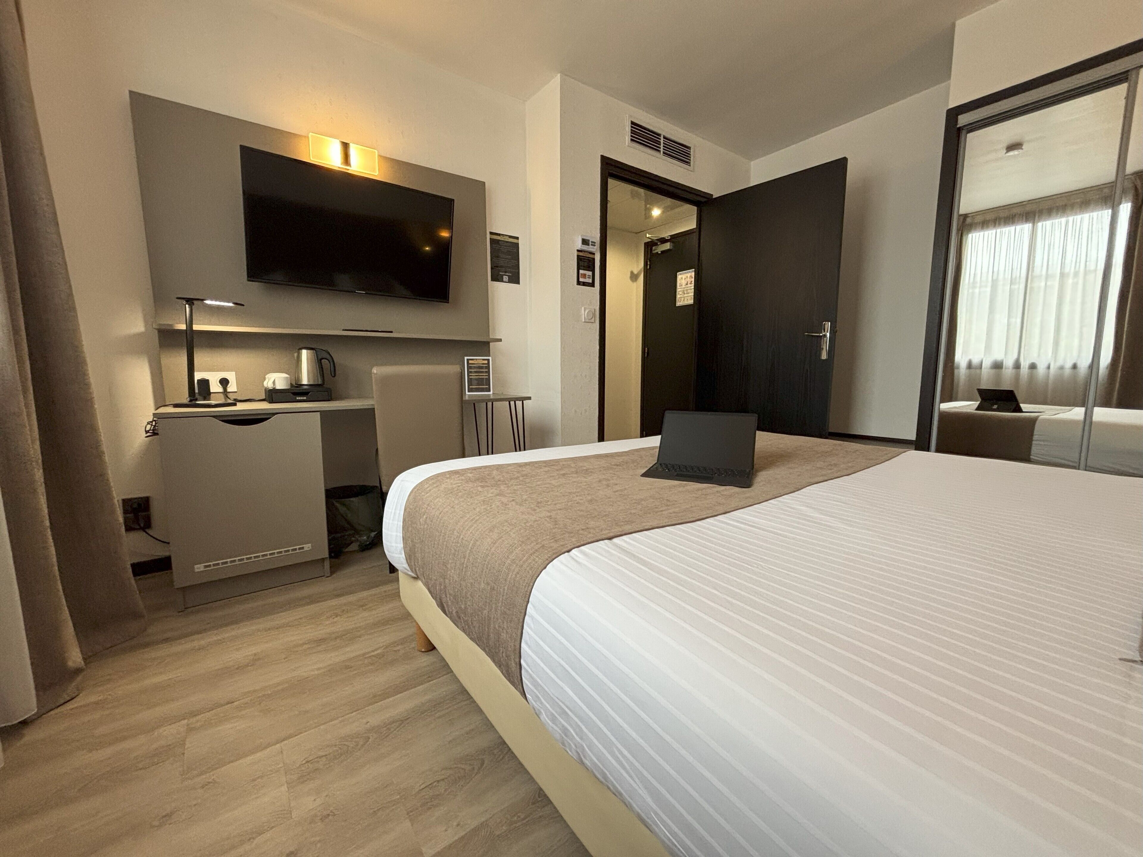 Una habitación de hotel con una cama grande, un escritorio con una computadora portátil, un televisor de pantalla plana y una pequeña mesa con cafetera.