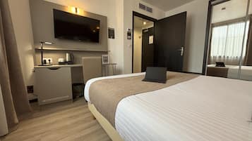Una habitación de hotel con una cama grande, un escritorio con una computadora portátil, un televisor de pantalla plana y una pequeña mesa con cafetera.