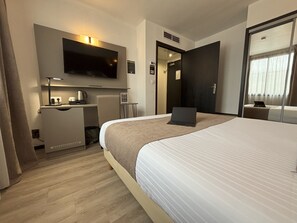 A hotel room with a large bed, a desk with a laptop, a flat-screen TV, and a small table with a coffee maker. - Hôtel Le Valois, Cognac (Cognac)