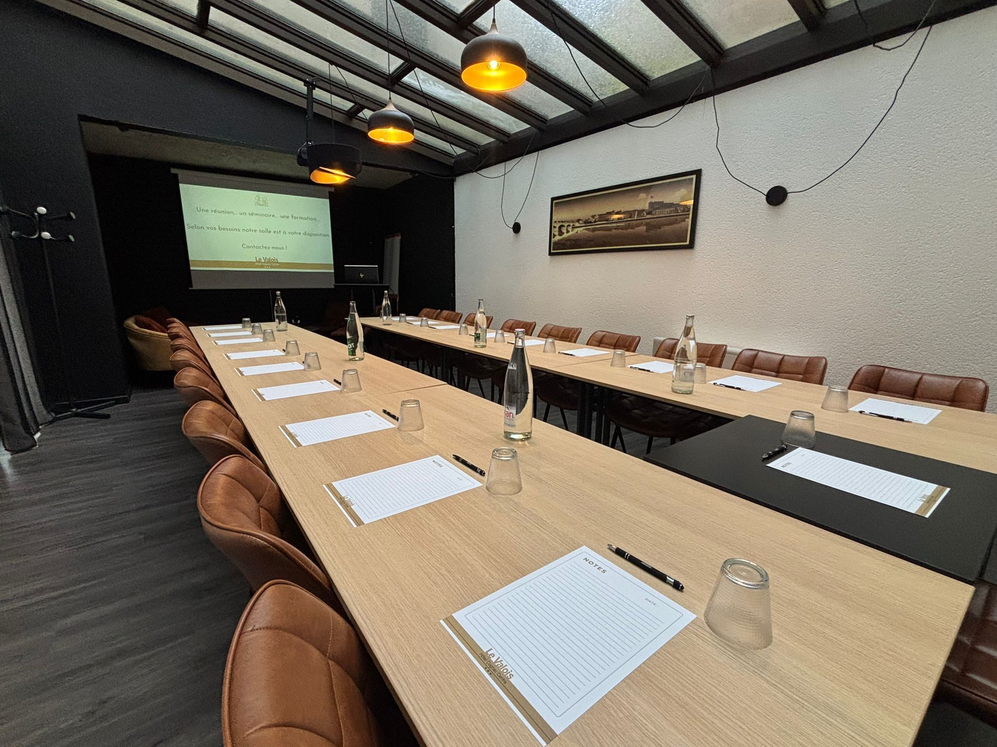 Una sala conferenze con lunghe tavolate, sedie e uno schermo per proiezioni.