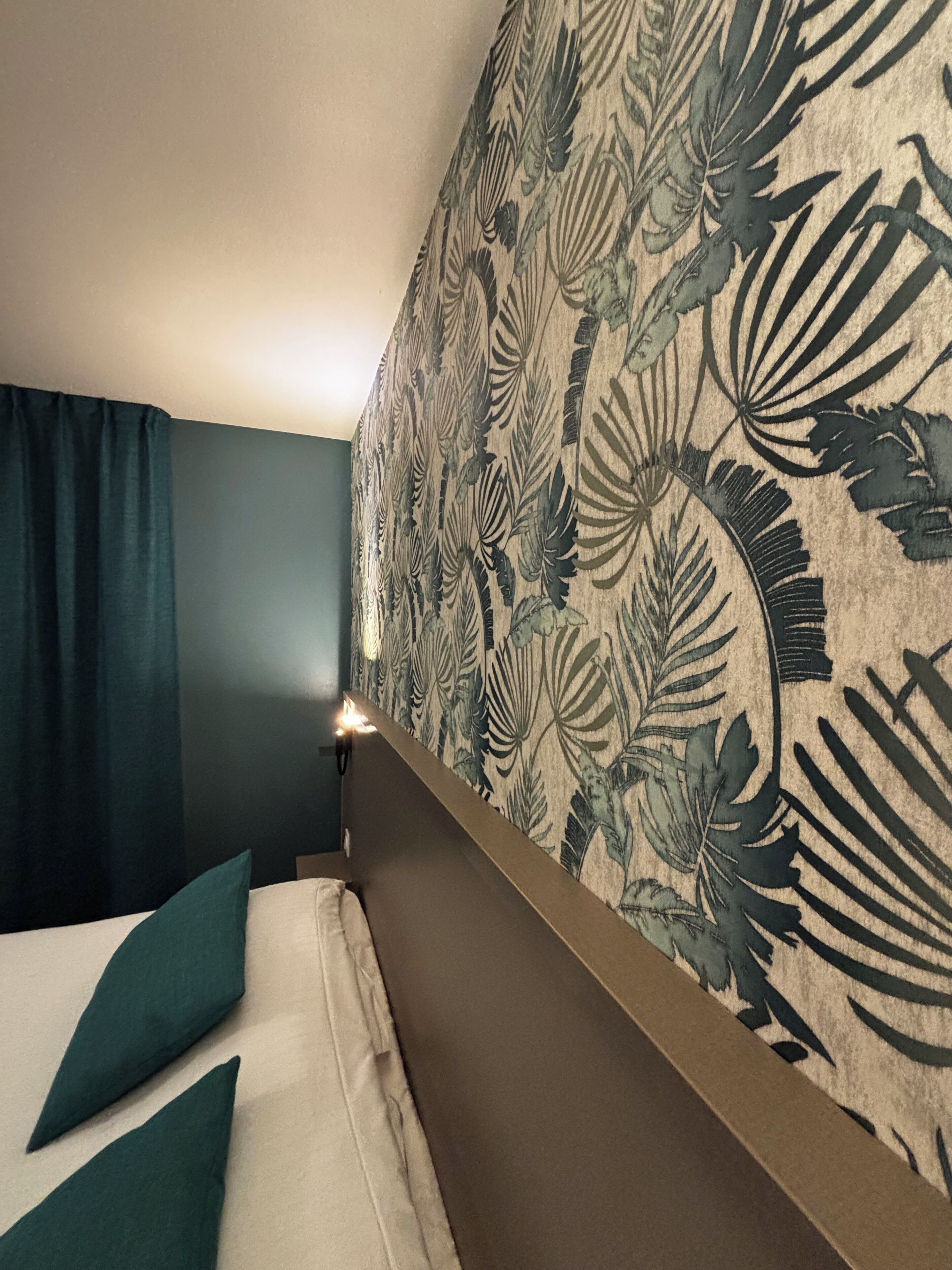 A hotel room with a bed, dark curtains, and a floral-patterned headboard.