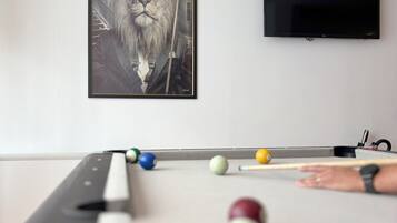 A billiards table with balls and a cue stick, a framed portrait on the wall, and a flat-screen TV.