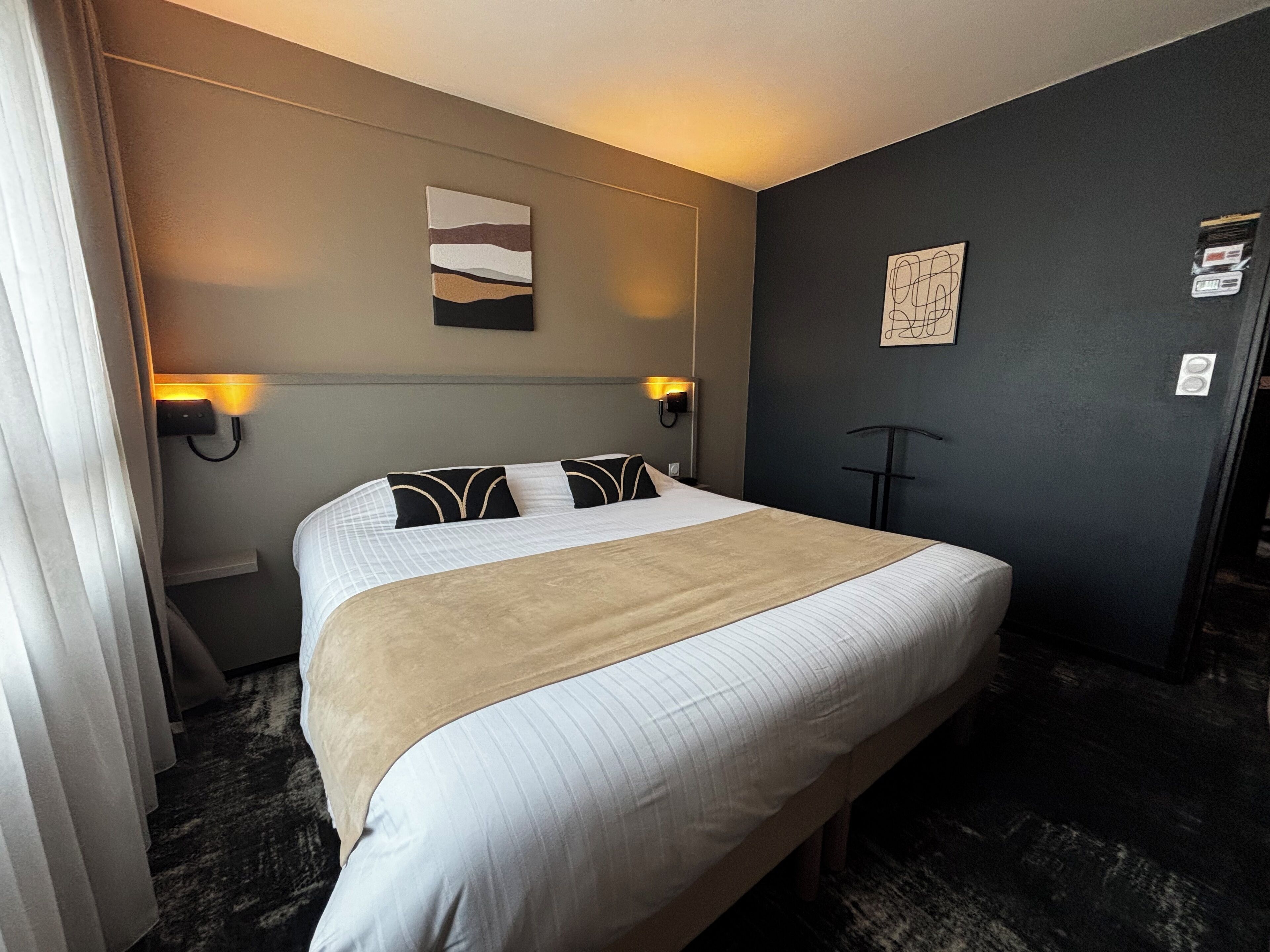 A hotel room with a large bed, two bedside lamps, a headboard, a wall-mounted artwork, and a door.