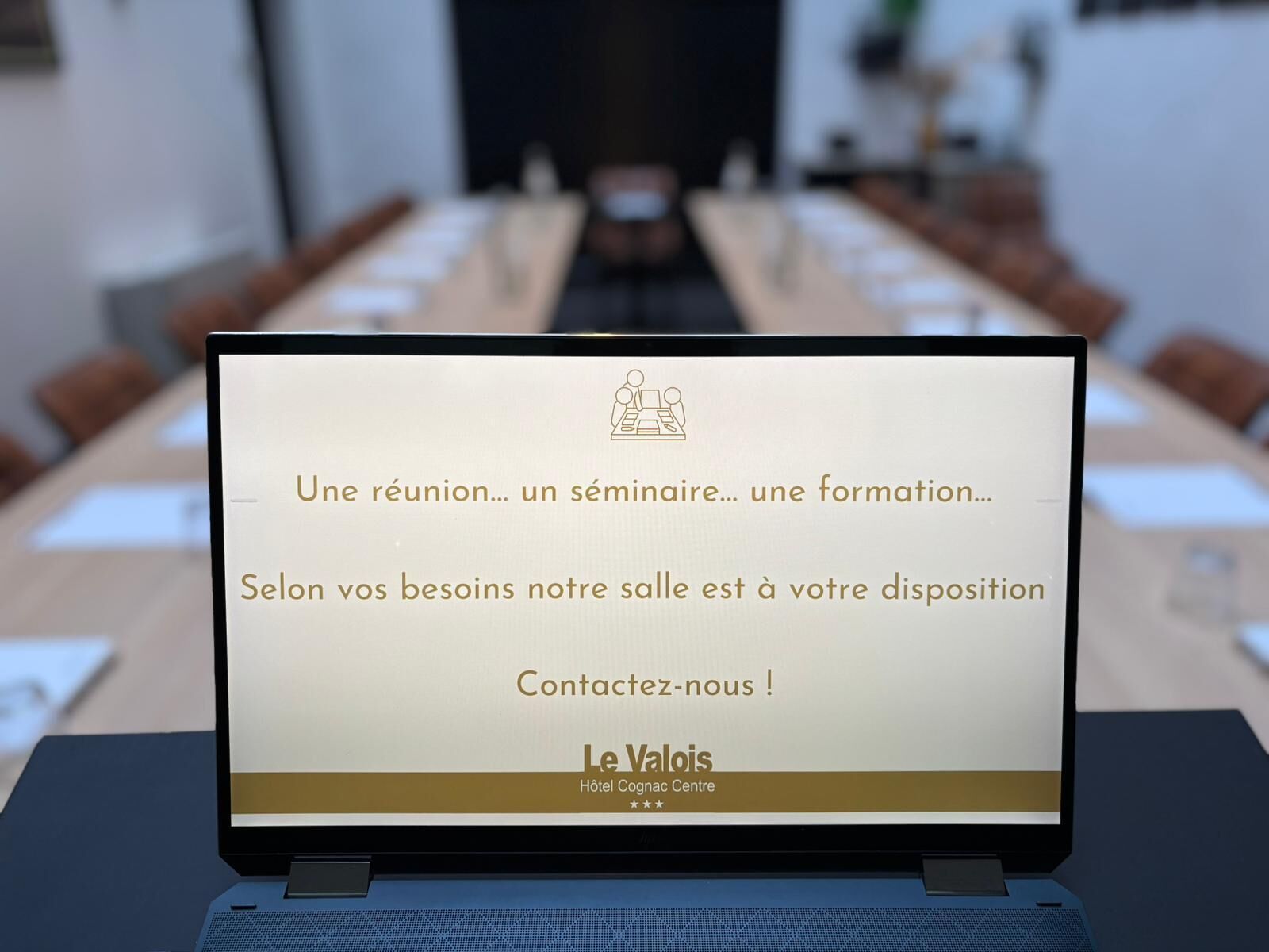 Een laptop op een tafel waarop een bericht staat over een vergadering, seminar of training, met een logo voor Le Valois Hotel Cognac Centre.