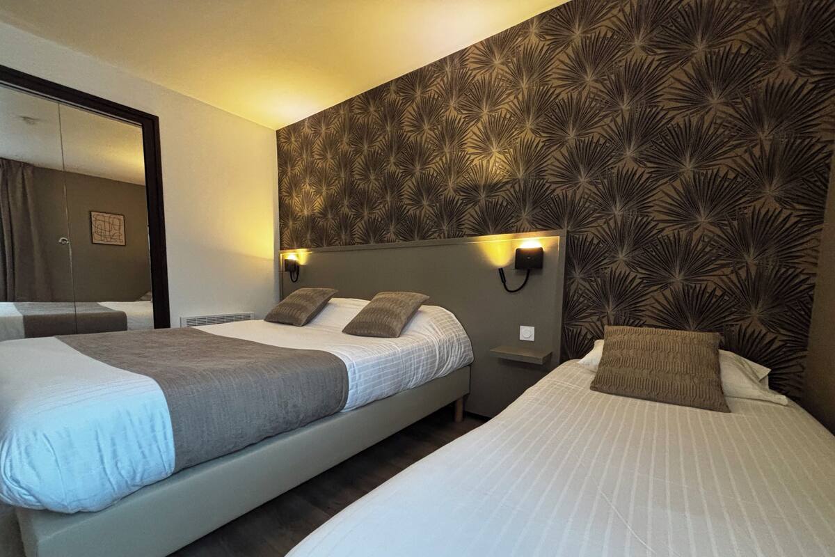 A hotel room with two beds, a large mirror, and a patterned wall.