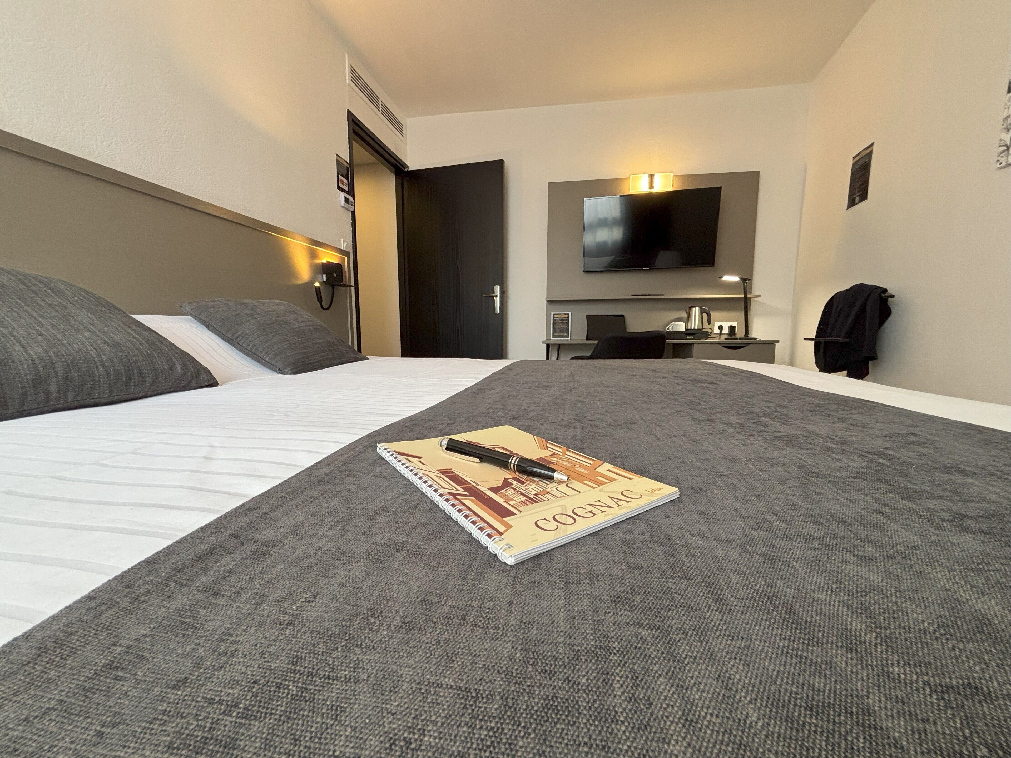 Una habitación de hotel con cama, escritorio, televisor y perchero.