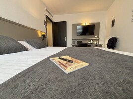 Una habitación de hotel con cama, escritorio, televisor y perchero.