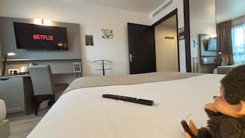 A hotel room with a bed, a desk with a chair, a TV displaying 'NETFLIX', and a door leading to another room.
