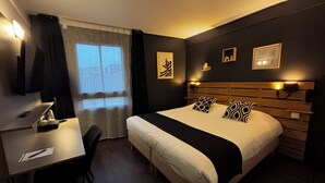 A hotel room with a bed, bedside tables, a desk, a chair, and a window with curtains.