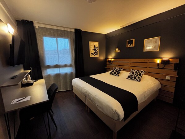Habitación de hotel con cama, mesitas de noche, escritorio, silla y ventana con cortinas.