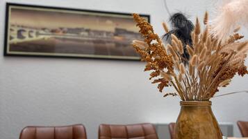 A conference room with a table, chairs, a vase with dried plants, and a framed picture on the wall.