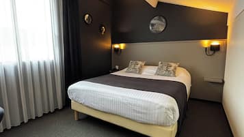 Quarto de hotel moderno com cama grande, paredes escuras e duas luminárias fixadas na parede.