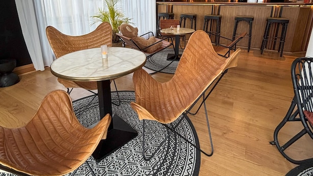 A modern bar area with round tables and wicker chairs, a patterned rug, and a bar counter with bottles.