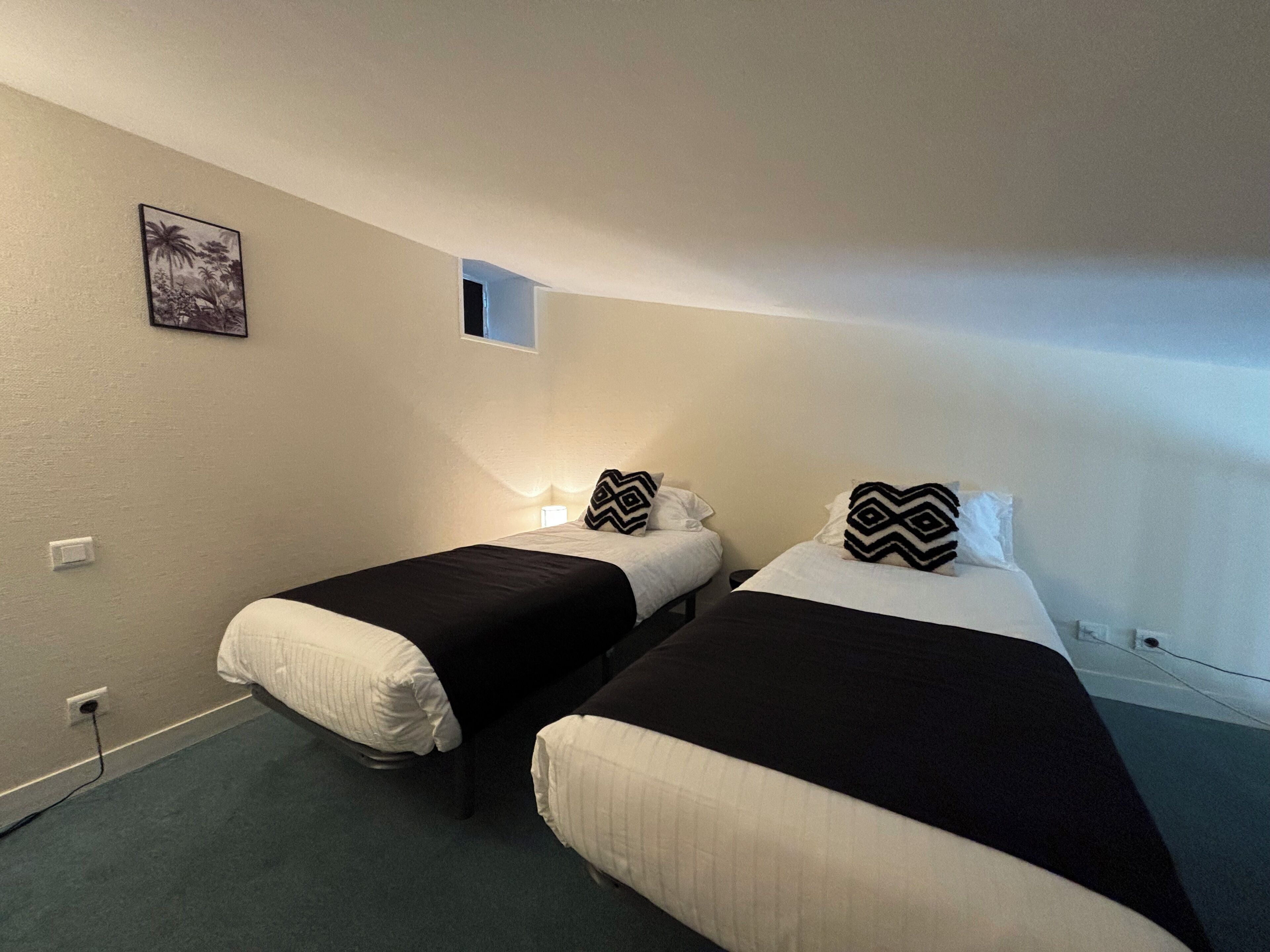 A small, dimly lit room with two beds, each with a black and white patterned pillow, and a small window.