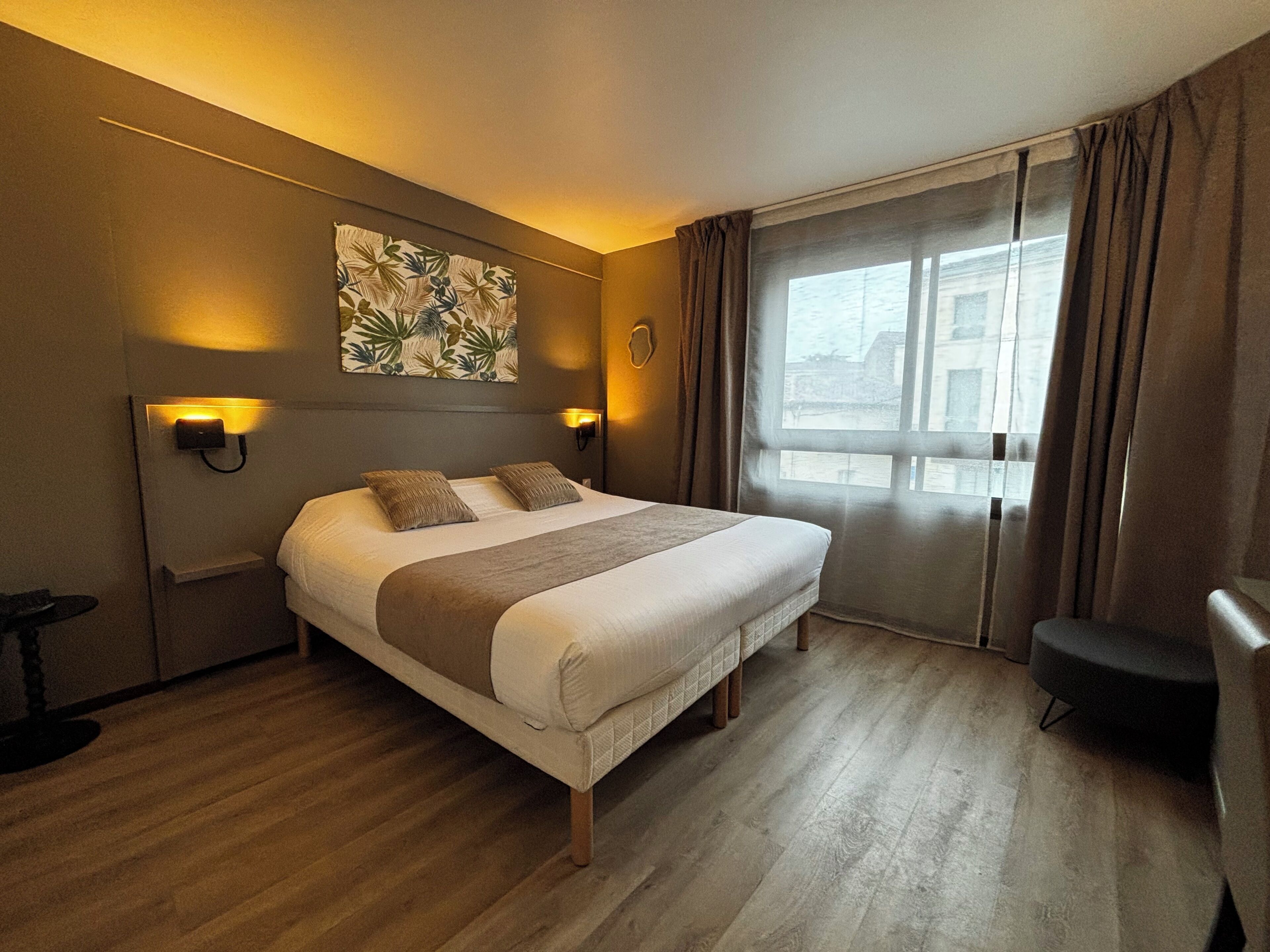 A hotel room with a large bed, bedside lamps, a window with curtains, and a wall-mounted artwork.