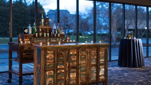 A bar area with a wooden cabinet filled with bottles and glasses, a chair, and a table with a dark cloth. - Sonesta Nashville Airport (Nashville)