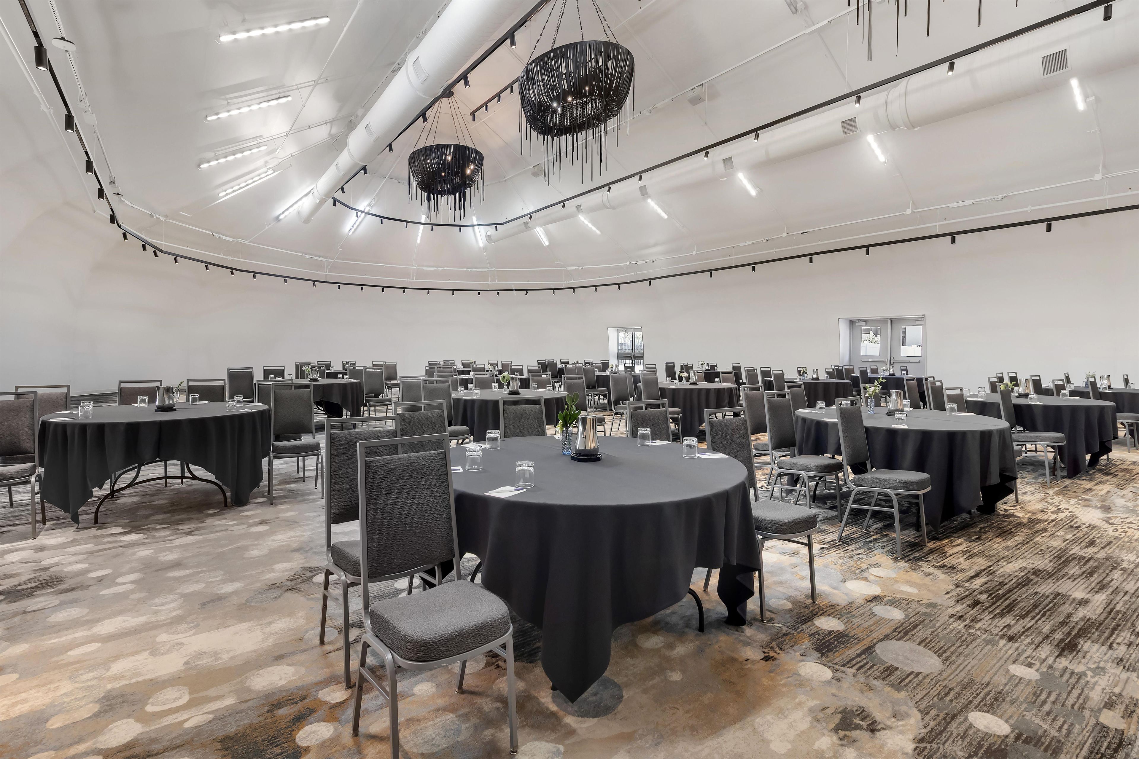 A large conference room with multiple round tables, chairs, and a modern chandelier.