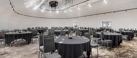 A large conference room with multiple round tables, chairs, and a modern chandelier.