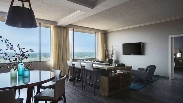 A modern hotel room with a dining area, a sofa, a TV, and a large window with a view. - Sonesta Nashville Airport (Nashville)