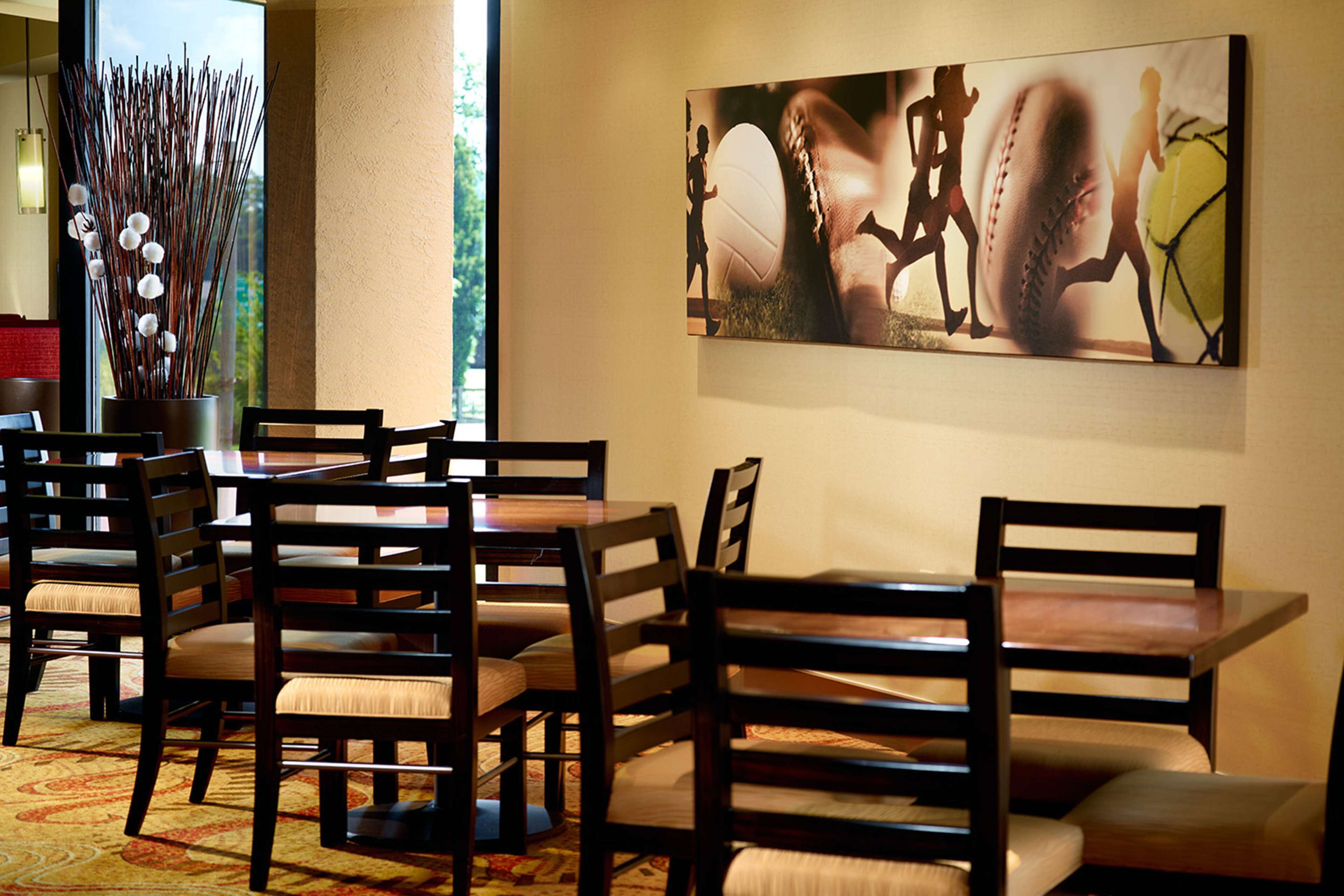 Un comedor con mesas y sillas de madera, un ventanal con vistas y una obra de arte colgada en la pared.