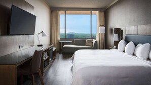 A hotel room with a large bed, a desk with a chair, a television, a sofa, and a window with a city view. - Sonesta Nashville Airport (Nashville)