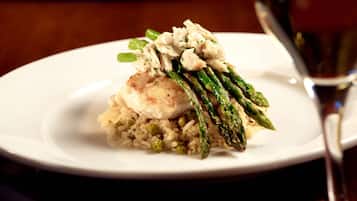 A plate of food with rice, peas, asparagus, and a piece of meat, accompanied by a glass of wine.